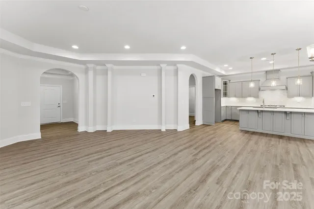 a view of an empty room with wooden floor and a kitchen