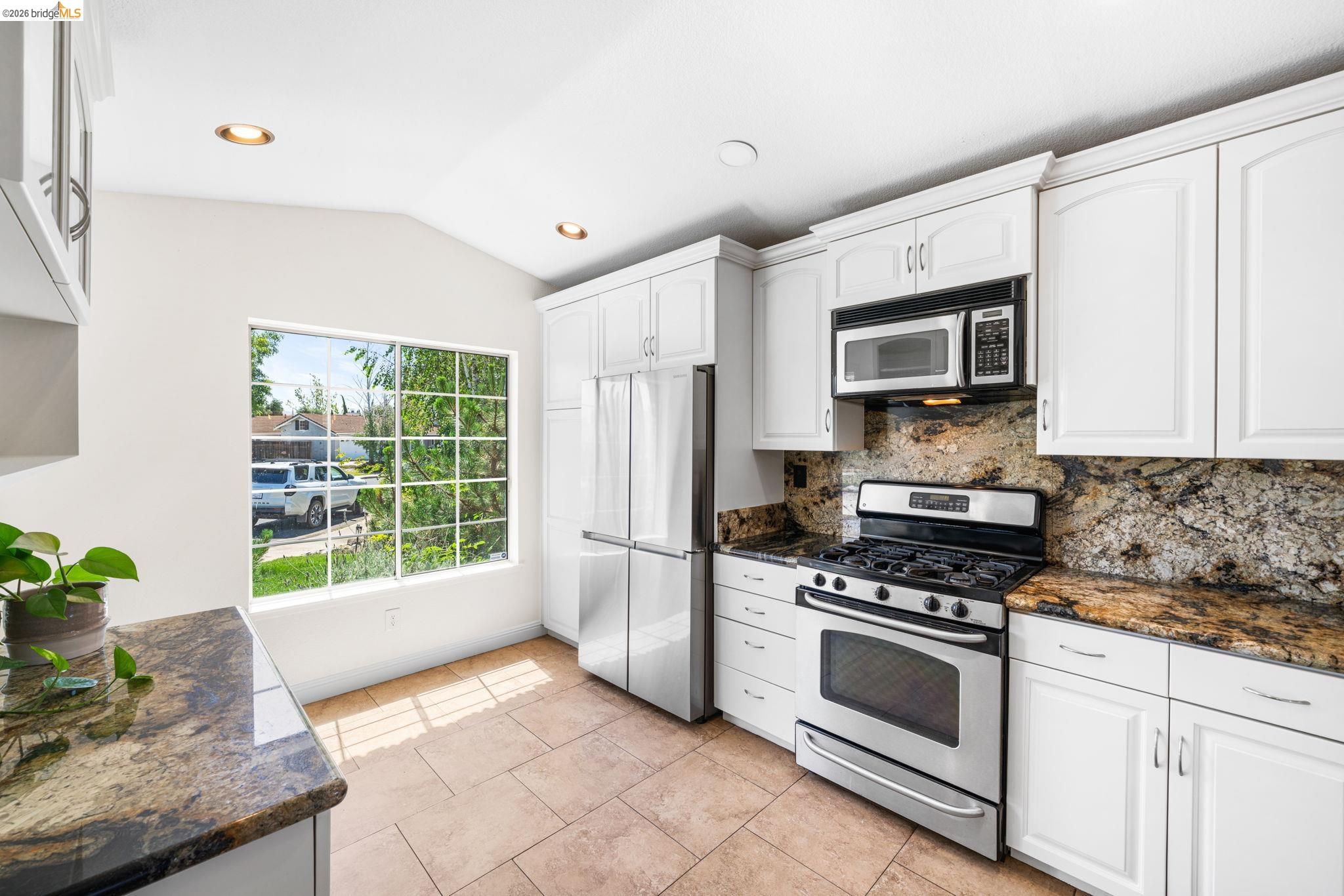 1186 El Rio Court Livermore, CA 94551 - Photo 16 of 60 Bright kitchen featuring white cabinetry, stainless steel appliances, granite countertops, and a tiled backsplash