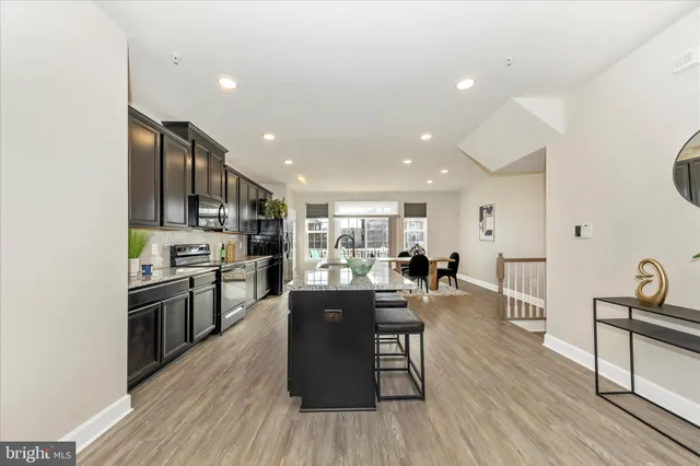 a kitchen with stainless steel appliances kitchen island granite countertop a stove top oven a sink a dining table and chairs with wooden floor