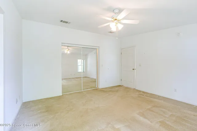 an empty room with chandelier fan and windows