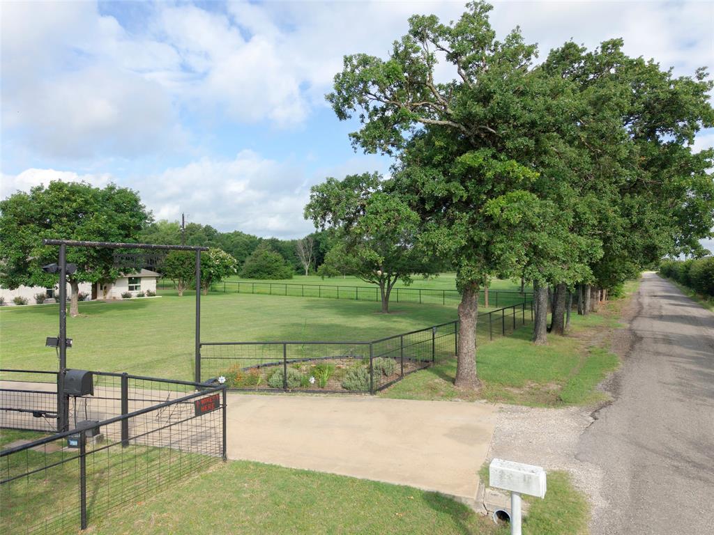 380 Farr Altom Road Seagoville, TX 75159 - Photo 24 of 30 Gated property entrance with a paved driveway, featuring mature trees lining the perimeter and a manicured lawn