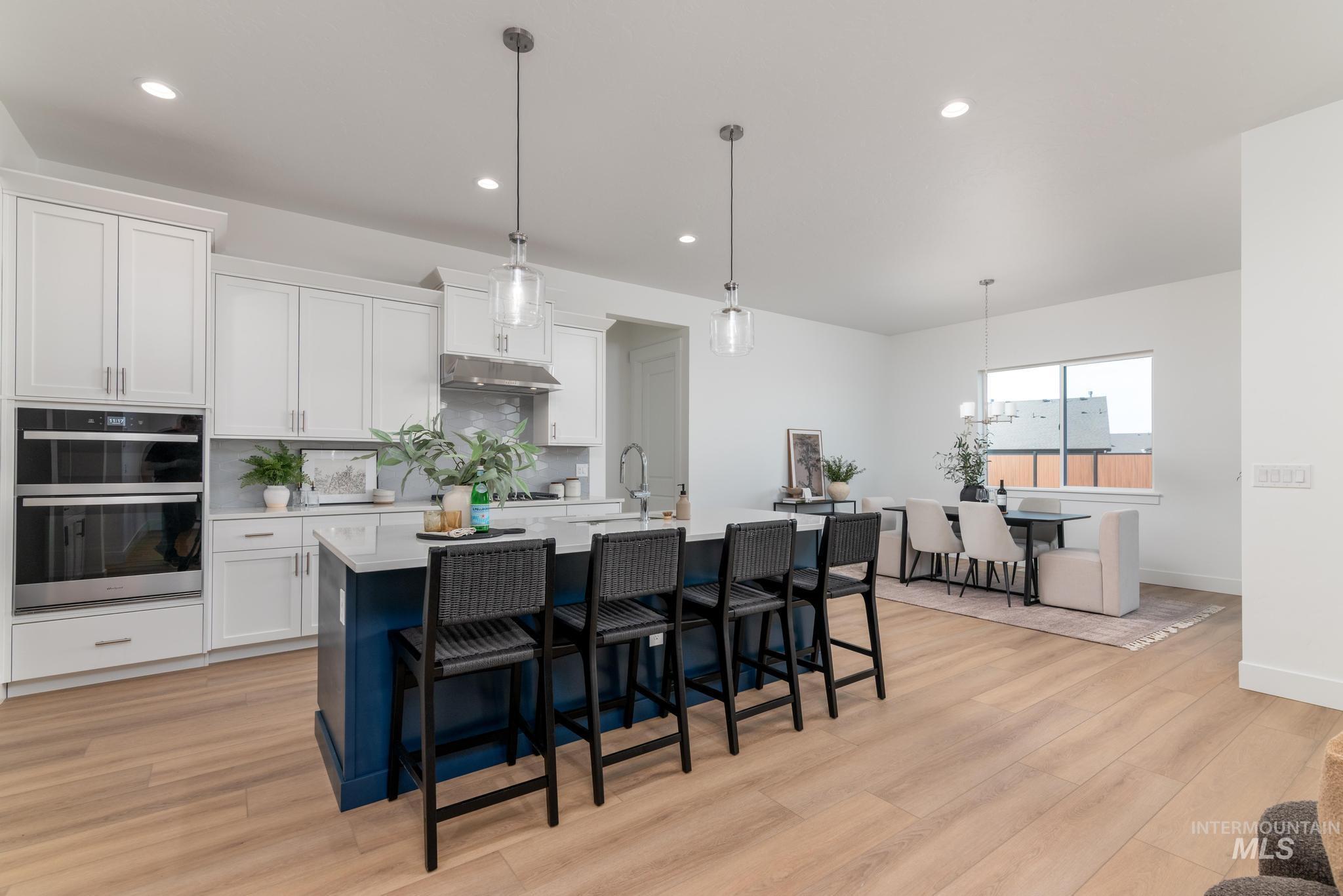 3612 North Pindall Way Star, ID 83669 - Photo 4 of 12 Two tone kitchen featuring pendant lighting, a kitchen bar, backsplash, stainless steel double oven, and light wood-style floors