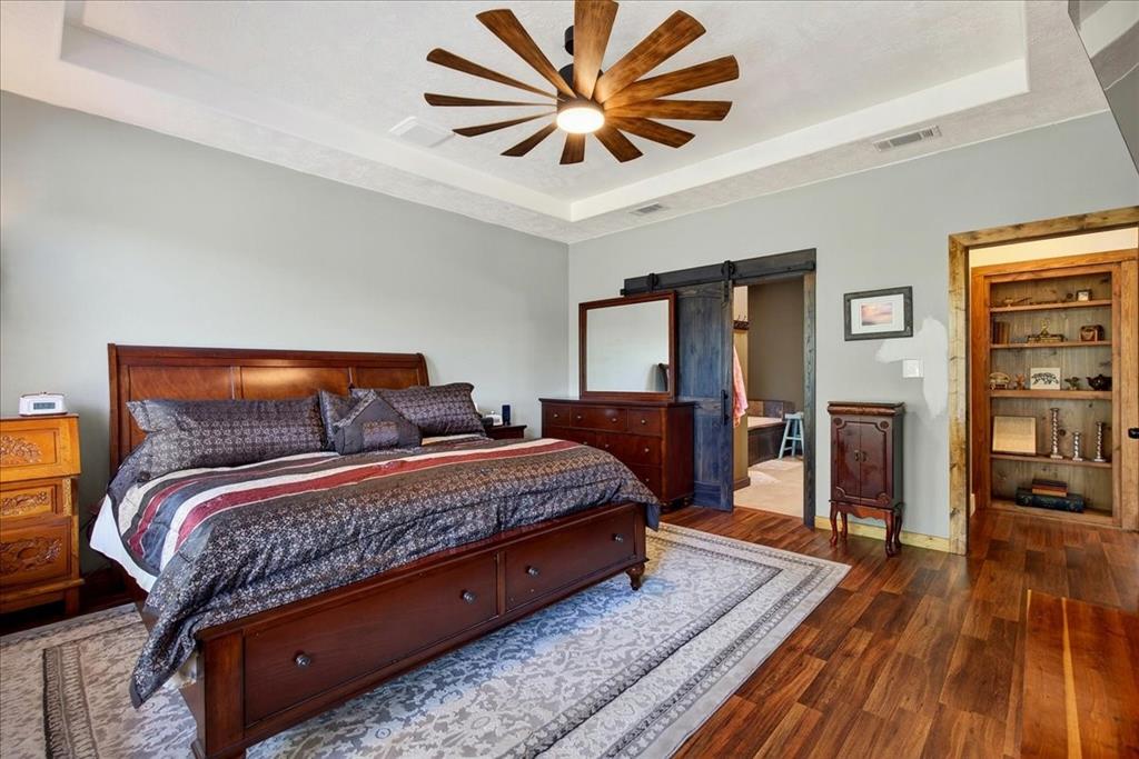 11591 Farm To Market 59 Athens, TX 75751 - Photo 13 of 40 Primary Bedroom featuring wood-finish flooring, a tray ceiling with a farm-style ceiling fan, and a barn door entry