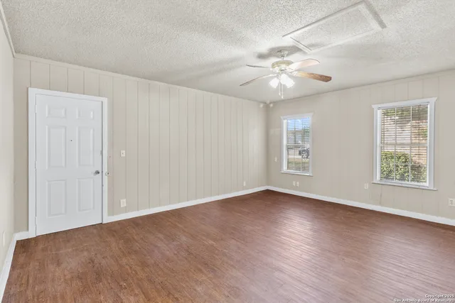 an empty room with wooden floor chandelier fan and windows