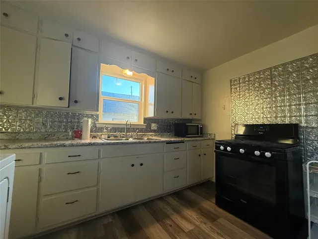 a kitchen with granite countertop a stove a sink dishwasher and white cabinets with wooden floor