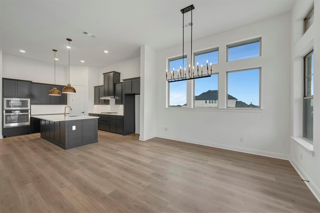 8712 Chestnut Lane Justin, TX 76247 - Photo 12 of 29 Kitchen featuring a center island with sink, a chandelier, stainless steel appliances, light wood-style floors, and tasteful backsplash
