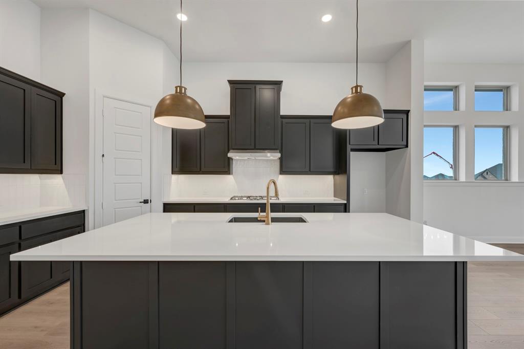 8712 Chestnut Lane Justin, TX 76247 - Photo 6 of 29 Kitchen with light wood-style floors, an island with sink, light stone counters, and decorative light fixtures