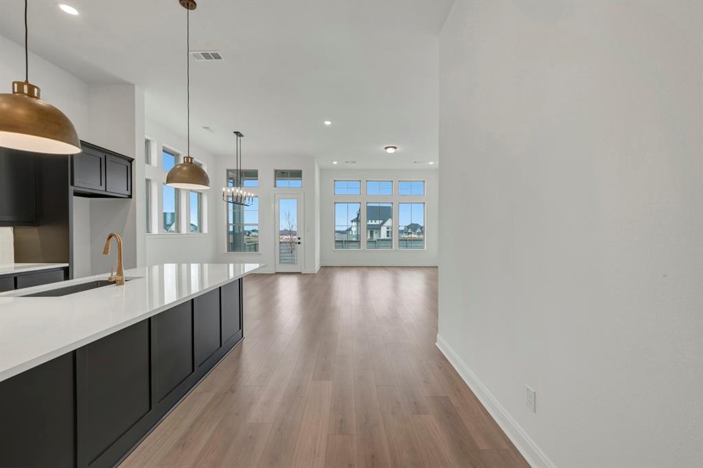 8712 Chestnut Lane Justin, TX 76247 - Photo 7 of 29 Kitchen featuring light stone counters, light wood-style flooring, dark cabinets, and hanging light fixtures