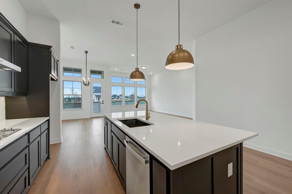 8712 Chestnut Lane Justin, TX 76247 - Photo 9 of 29 Kitchen featuring a kitchen island with sink, dishwasher, light wood-style floors, hanging light fixtures, and light stone counters