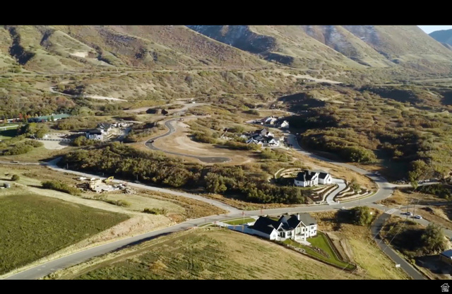 89 East Mapleton Estates Drive, Unit 99102 Mapleton, UT 84664 - Photo 2 of 8 Expansive mountain landscape with winding roads and scattered residential properties, featuring a foreground property with a white picket fence, manicured lawn, and a paved driveway