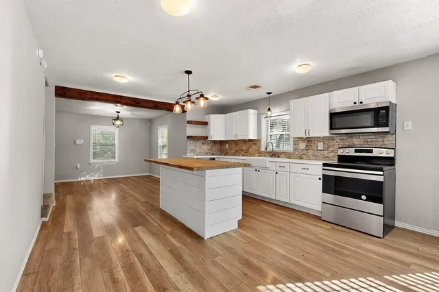 a kitchen with stainless steel appliances granite countertop hardwood a sink dishwasher a stove and white cabinets with wooden floor