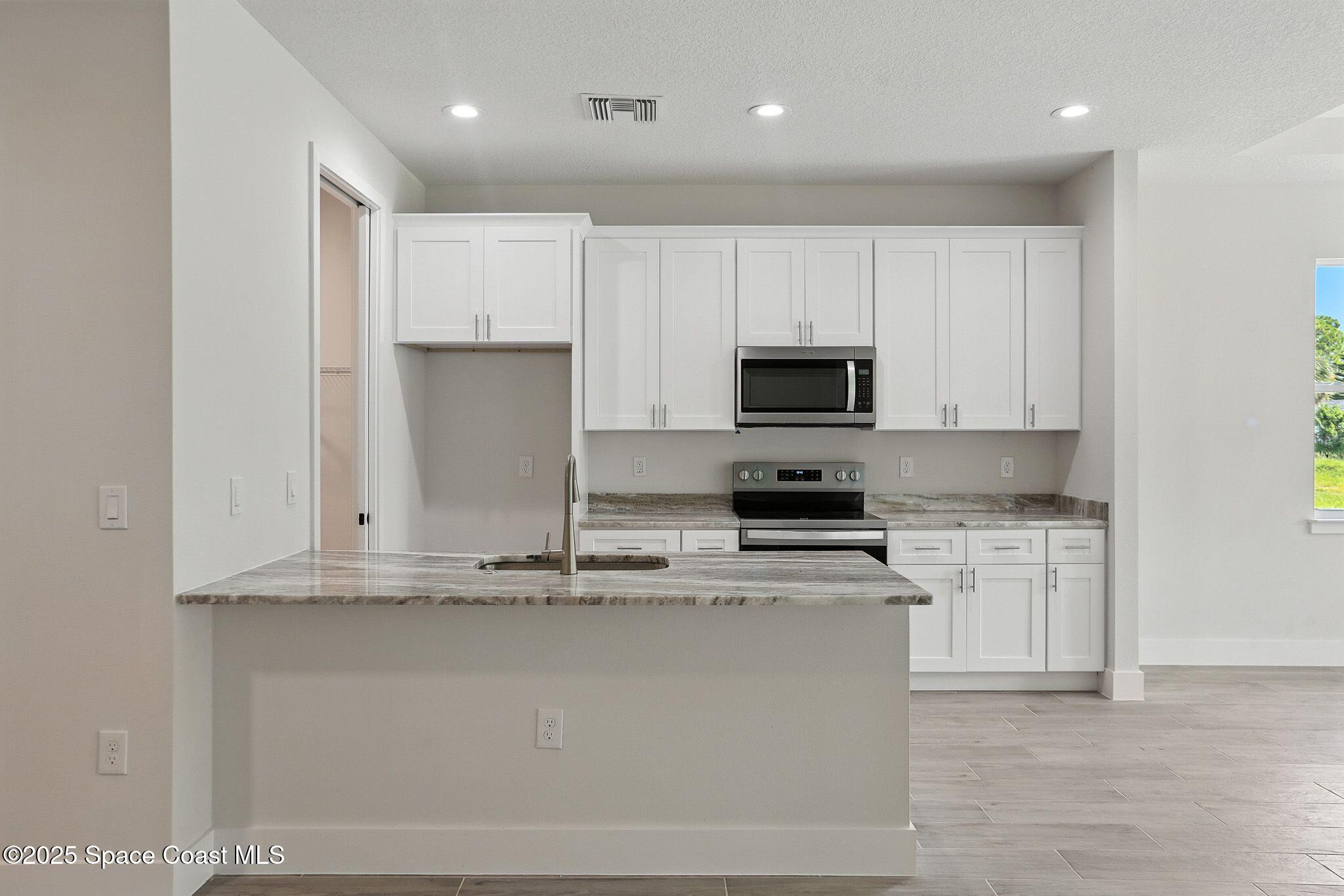 475 Flagler Road Southeast Palm Bay, FL 32909 - Photo 11 of 30 a kitchen with kitchen island granite countertop a stove top oven a sink and white cabinets