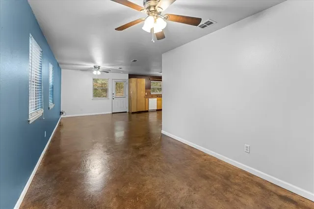 an empty room with wooden floor kitchen view and a window
