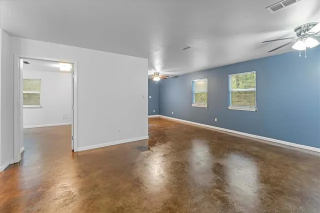 an empty room with wooden floor chandelier fan and windows