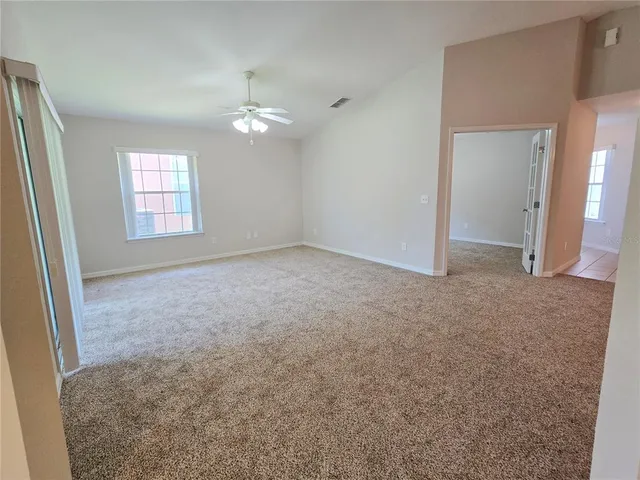 an empty room with a chandelier fan and windows