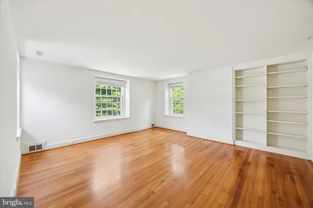 an empty room with wooden floor closet and windows