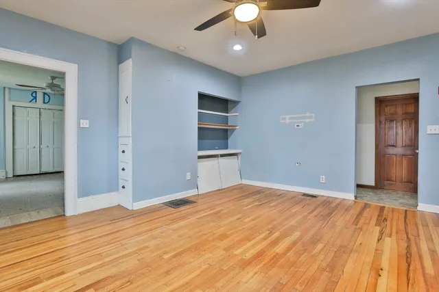 an empty room with wooden floor and way to kitchen