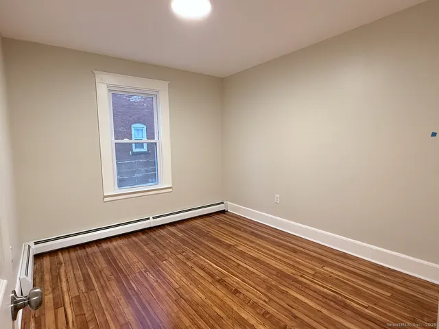 a view of an empty room with window and wooden floor