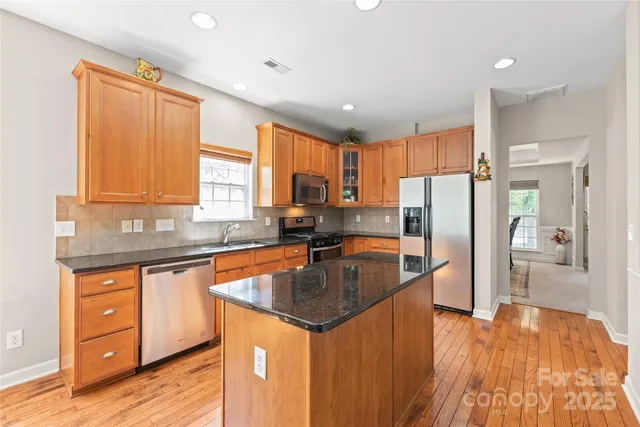 a kitchen with stainless steel appliances granite countertop a refrigerator a sink dishwasher a stove and white countertops with wooden floor