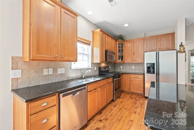 a kitchen with stainless steel appliances granite countertop a refrigerator a sink dishwasher a stove with wooden cabinets and floor