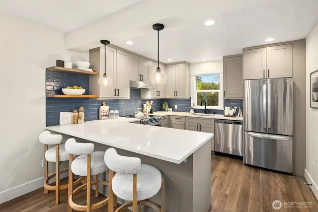 a kitchen with stainless steel appliances kitchen island granite countertop a refrigerator a stove and white cabinets with wooden floor