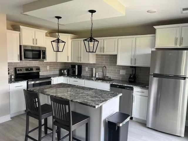 a kitchen with stainless steel appliances granite countertop a sink a stove a refrigerator cabinets a dining table and chairs