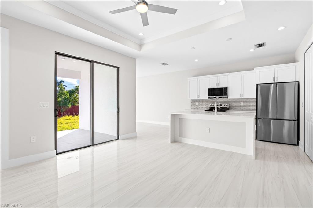 2064 55th Terrace Southwest Naples, FL 34116 - Photo 25 of 30 Kitchen with stainless steel appliances, a center island with sink, white cabinetry, a raised ceiling, and recessed lighting