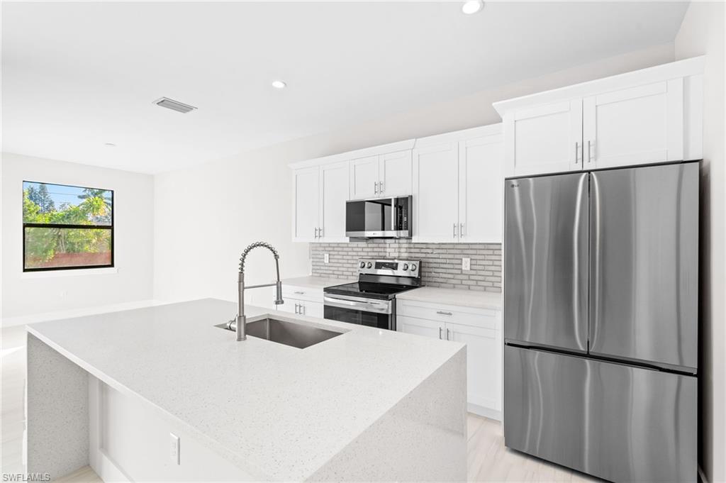 2064 55th Terrace Southwest Naples, FL 34116 - Photo 5 of 30 Kitchen featuring stainless steel appliances, light stone countertops, white cabinets, a kitchen island with sink, and decorative backsplash