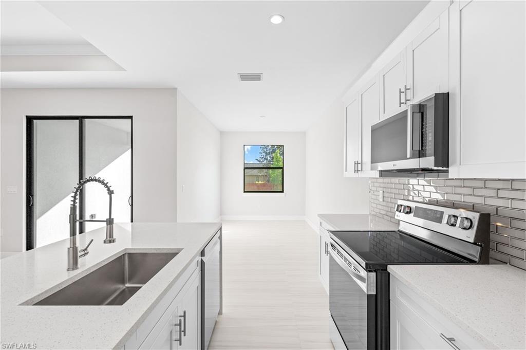 2064 55th Terrace Southwest Naples, FL 34116 - Photo 6 of 30 Kitchen featuring stainless steel appliances, white cabinetry, light stone countertops, recessed lighting, and decorative backsplash