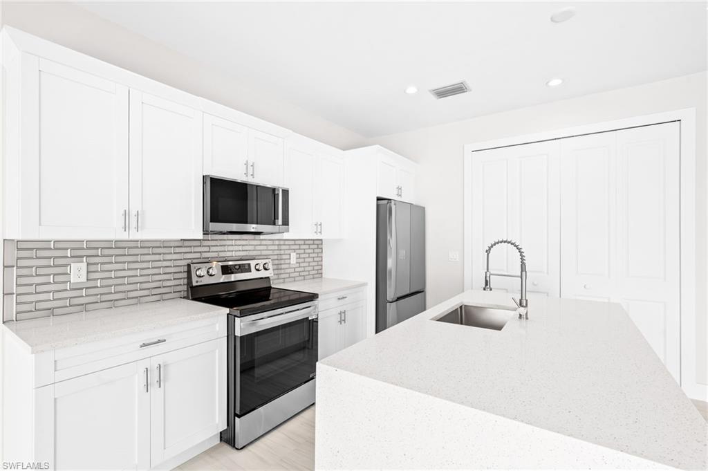 2064 55th Terrace Southwest Naples, FL 34116 - Photo 7 of 30 Kitchen featuring stainless steel appliances, light stone counters, white cabinets, and recessed lighting