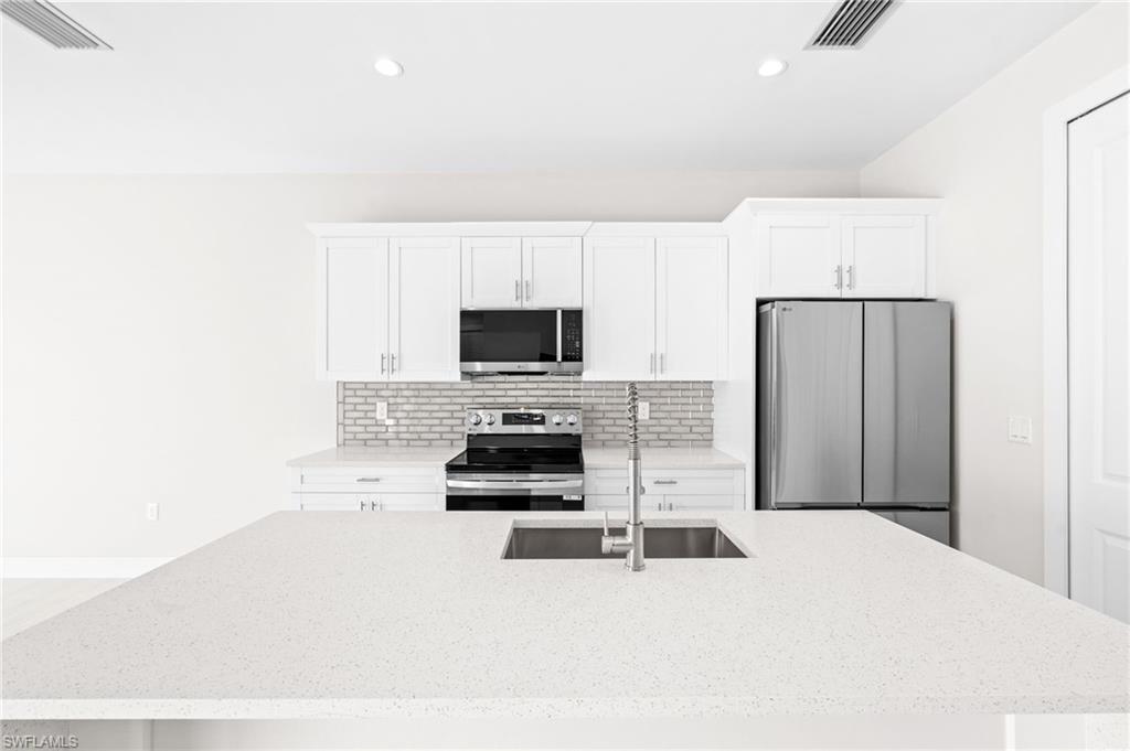 2064 55th Terrace Southwest Naples, FL 34116 - Photo 8 of 30 Kitchen with stainless steel appliances, an island with sink, light stone countertops, white cabinets, and recessed lighting