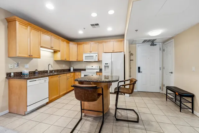 a kitchen with stainless steel appliances granite countertop a stove a sink a refrigerator and white cabinets with wooden floor