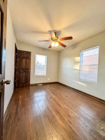 a view of an empty room with wooden floor and a ceiling fan