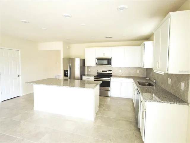 a large kitchen with kitchen island granite countertop a sink and white cabinets