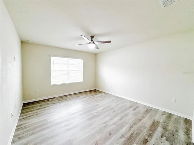 an empty room with wooden floor chandelier fan and windows