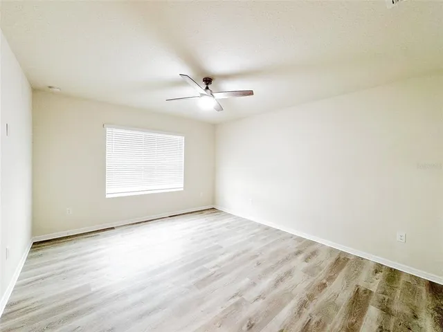 an empty room with wooden floor chandelier fan and windows