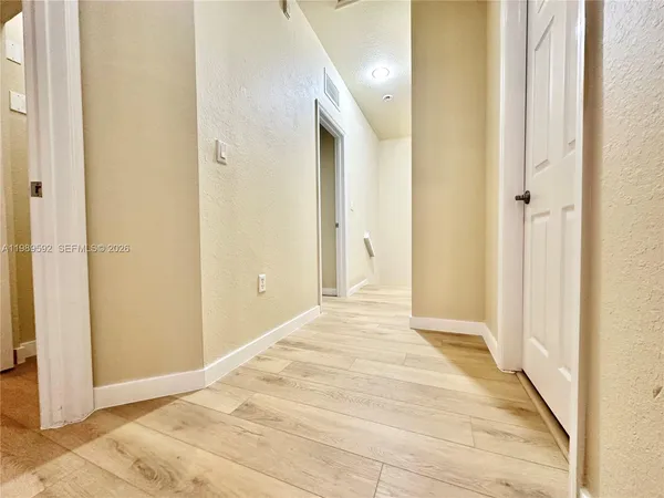 a view of a hallway with wooden floor and a bathroom