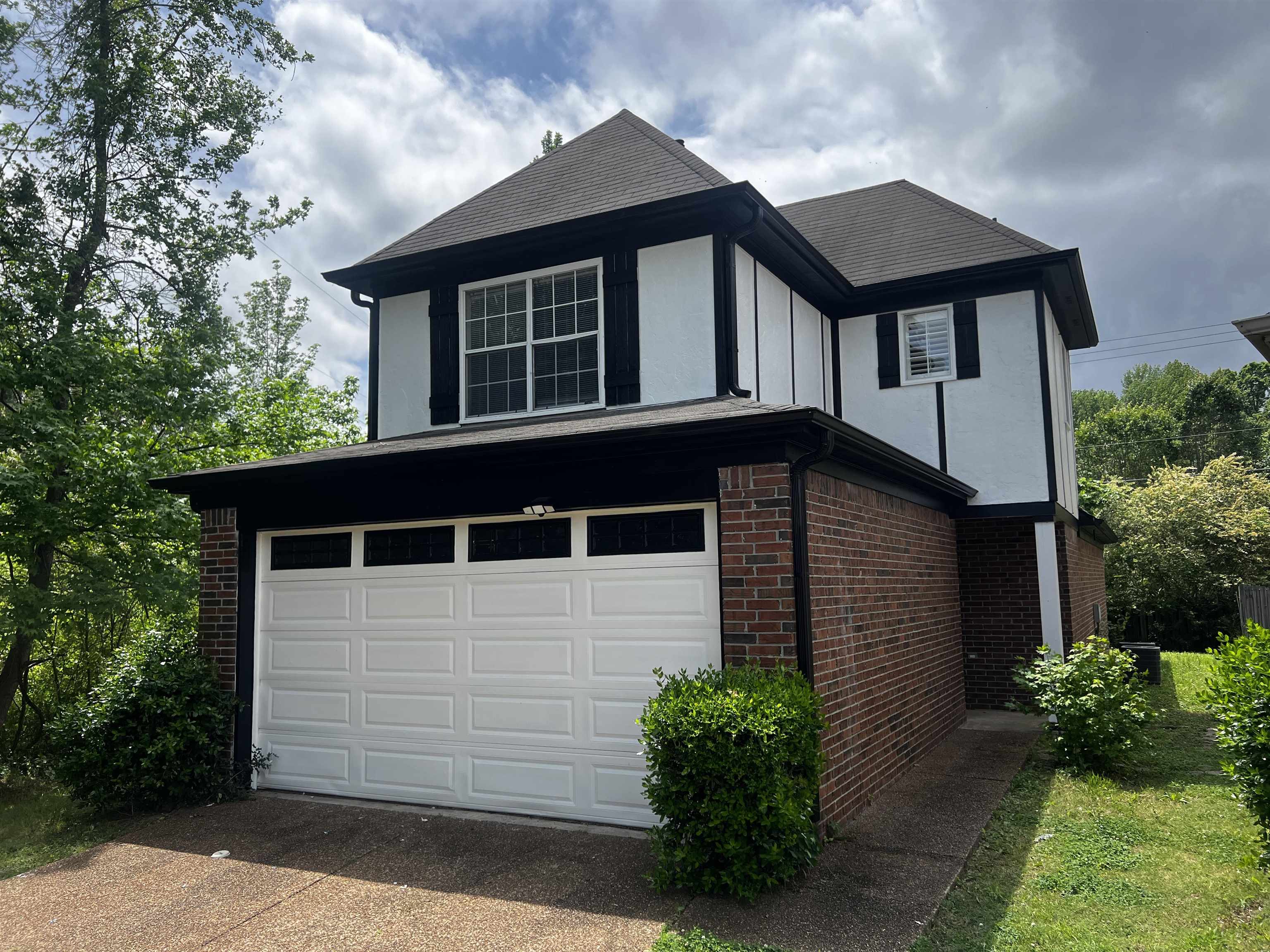 View of side of home featuring driveway, brick siding, a garage, and stucco siding
