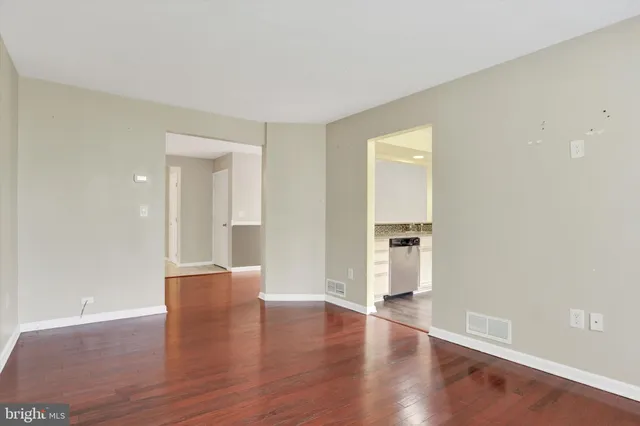 a view of empty room with wooden floor and kitchen