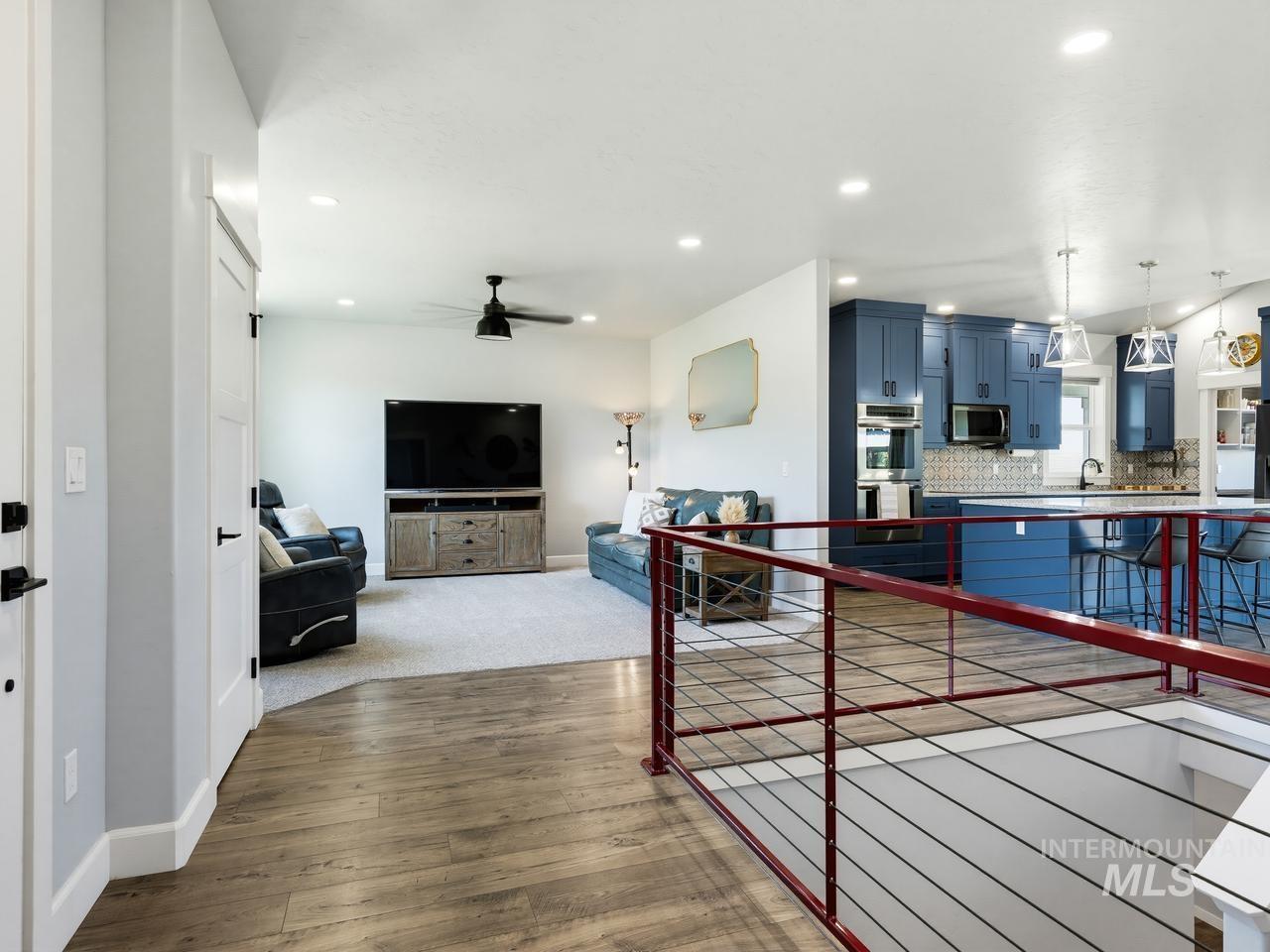 4950 West Columbia Road Nampa, ID 83687 - Photo 7 of 50 Open-concept living space featuring wood-finish flooring, a kitchen with blue cabinetry, a center island with pendant lighting, a built-in oven, and a contemporary railing system