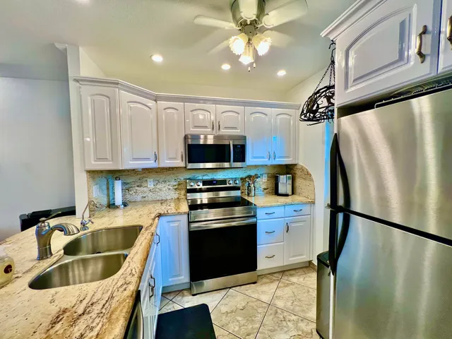 a kitchen with stainless steel appliances granite countertop a refrigerator a sink a stove with white cabinets