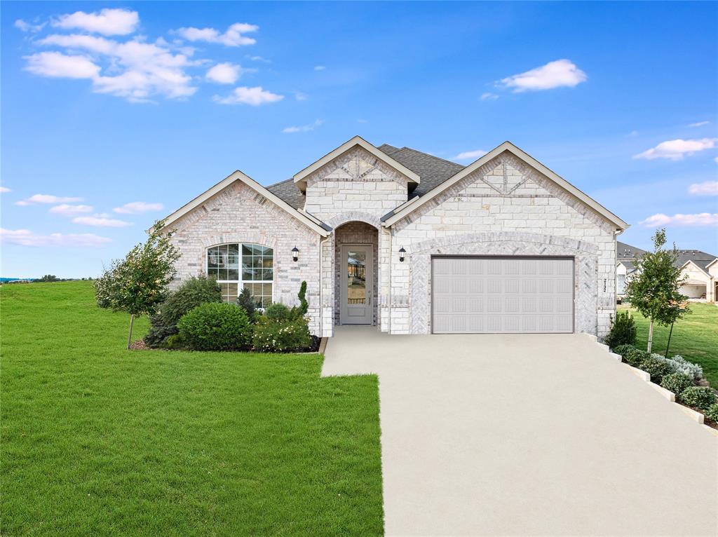 French country inspired facade featuring a front yard, concrete driveway, an attached garage, stone siding, and brick siding