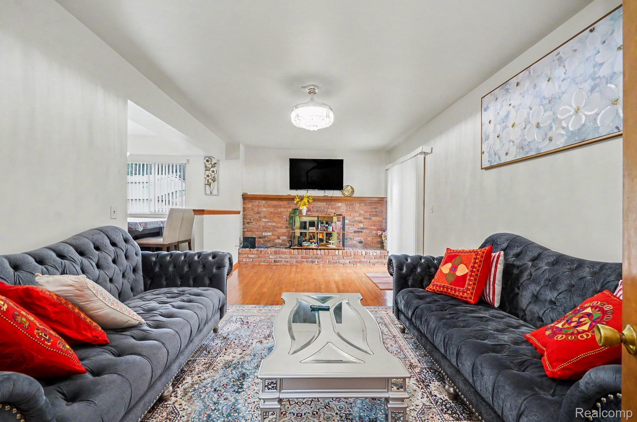 6653 Flintlock Ridge Utica, MI 48317 - Photo 13 of 31 Living room featuring a brick fireplace with a wood mantel, hardwood flooring, and a decorative ceiling light fixture