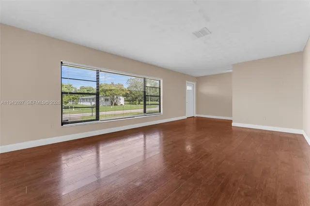a view of an empty room with wooden floor and a window