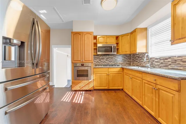 a kitchen with stainless steel appliances granite countertop a refrigerator a sink and wooden floors