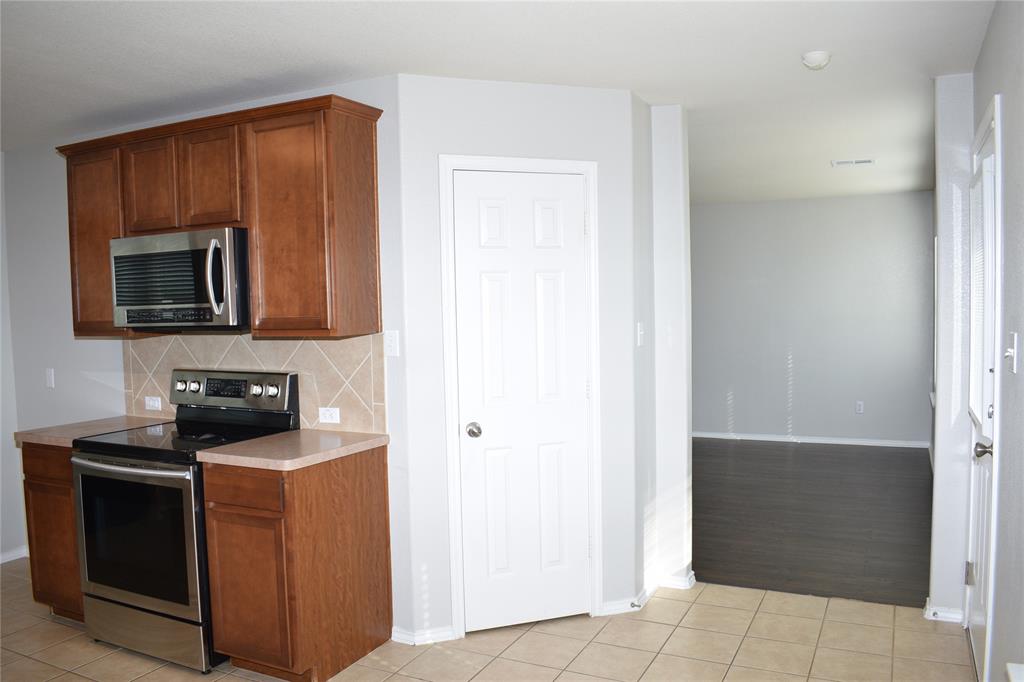 375 Housefinch Loop Leander, TX 78641 - Photo 6 of 28 Rich wood cabinetry and tile flooring anchor this functional kitchen area leading to living spaces.