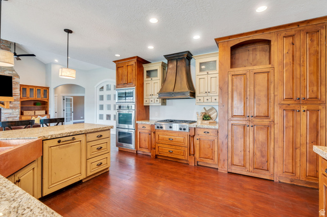 1355 West 1000 South Mapleton, UT 84664 - Photo 73 of 74 Two tone kitchen featuring arched walkways, hanging light fixtures, dark wood-style flooring, open floor plan, and light stone counters