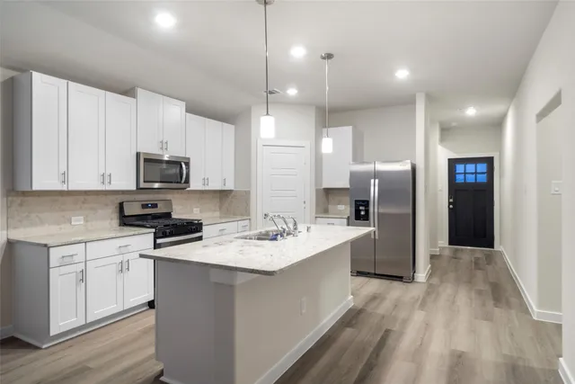 a kitchen with stainless steel appliances kitchen island a sink a stove a refrigerator and white cabinets with wooden floor