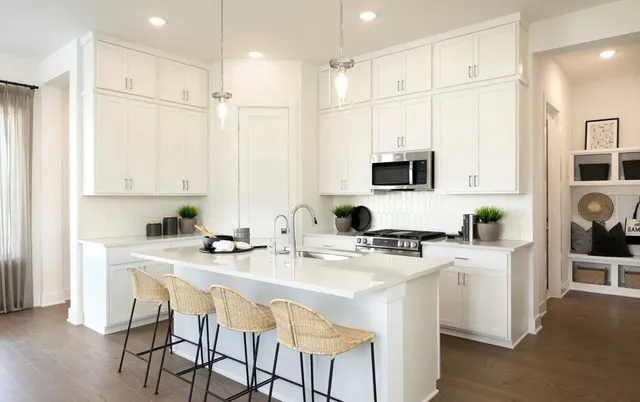 a kitchen with stainless steel appliances granite countertop a stove a sink a microwave a refrigerator and white cabinets with wooden floor