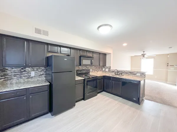 a kitchen with stainless steel appliances kitchen island granite countertop a refrigerator a sink dishwasher a oven with white cabinets and wooden floor